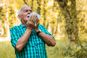 Older man sneezing as he stands out in nature