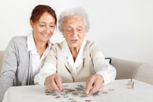 A daughter puts together a puzzle with her elderly mother, an activity that can help boost self-confidence in a loved one with dementia.