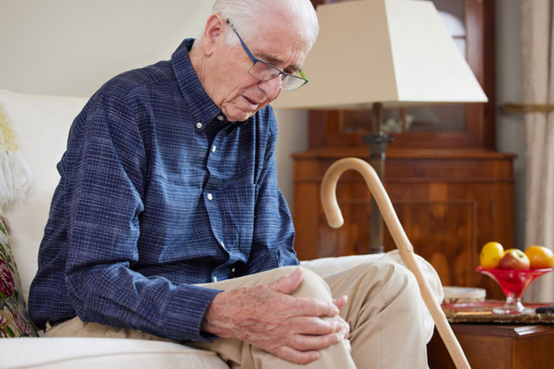 An older man rubs his knee as he prepares for joint replacement surgery.
