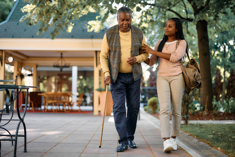 A woman helps her father walk while thinking about the obstacles family caregivers encounter.
