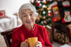 A senior woman drinks tea while sitting in her home decorated for the holidays. Remaining independent during aging is one of the many ways in-home care helps older loved ones.